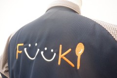 濃いネイビーの無地の背面にオレンジ色の糸と白糸で飲食や料理を連想させるオリジナルロゴ刺繍の制作事例のアップ。