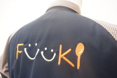 濃いネイビーの無地の背面にオレンジ色の糸と白糸で飲食や料理を連想させるオリジナルロゴ刺繍の制作事例のアップ。