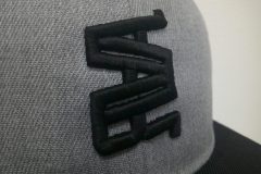 アッシュグレーの帽子の前面にアパレルブランドの太めのロゴ文字を黒糸で3D刺繍加工した制作事例のアップ。