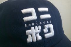 紺のコットンキャップの前面に白糸でオリジナル刺繍を加工した制作実績のアップ。カタカナ部分が3D刺繍。英字部分がサテン縫い。