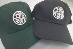 黒と緑のツイルキャップフロントに銀糸で社名ロゴをオリジナル3D刺繍として製作した作品実績を二つ並べたもの。