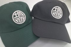 黒と緑のツイルキャップフロントに銀糸で社名ロゴをオリジナル3D刺繍として製作した作品実績を二つ並べたもの。