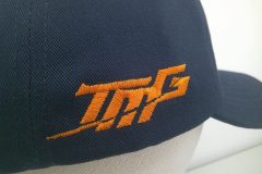 紺の帽子の右側面にスポーツチームのロゴを濃いオレンジの糸でサテン縫いで生成した制作実績。