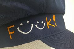 お持ち込みのキャスケットの右前面に白とオレンジの糸でシンプルに企業ロゴを刺繍した制作実例のアップ。
