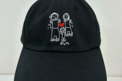 黒のキャップフロントに家族三人の温かなイラストが白糸と赤糸で刺繍された制作事例。