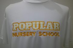白いTシャツにギンガムチェック柄の生地で英文字をカットし縁取り刺繡した制作事例。子供関連施設のスタッフユニフォーム。