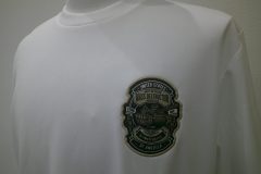 白Tシャツの左胸に楕円形に近い盾型の戦車のイラストがプリントされた生地を縁取り刺繍した制作事例。力強さと重厚感を感じさせる仕上がり。