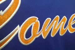 ブルーのベースボールシャツの背中にオレンジのエンブクロス生地をベースに白糸で縁取り刺繍を加工した制作事例のアップ。