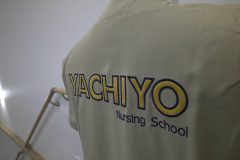 ベージュのスクラブの背中に医院名を縁取り刺繍した制作事例のアップ。ベース生地にはサテン地を使用。刺繍糸は濃紺。