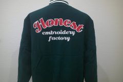 グリーンのメルトンジャケットの背中に店名を縁取り刺繍。赤のエンブクロス生地に白糸で縁取り。その下にはembroidery　factoryを白文字で直刺繍で加工した作品。