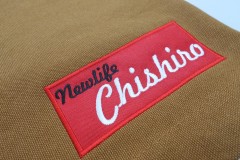 ワークエプロンの左すそに赤のボックスを縁取り刺繍。その上には黒糸と白糸で店名を刺繍した作品。