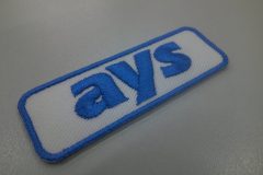白のツイル生地にサックスブルーの企業名を太めの文字で刺繍した、文字ワッペンの制作事例。