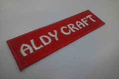 赤のエンブクロスに白糸で工房名をシンプルに刺繍した文字ワッペンの制作事例。