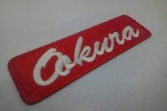 赤のエンブクロス生地に白糸で会社名を刺繍した文字ワッペン。書体はBrush Scriptを使用。