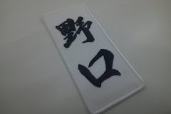 縦書きのレイアウトで個人名を刺繍した文字ワッペン。白のツイル生地に黒糸で刺繍。