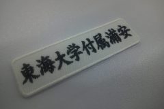 白の生地に黒糸で学校名を刺繍した、文字ワッペンの加工事例。