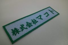水色のエンブクロス生地に緑の糸で会社名を刺繍した、文字ワッペンの制作事例。
