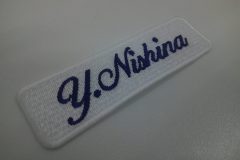 白の生地に人気の筆記体で個人名を刺繍した、文字ワッペンの加工事例。