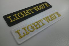 白の生地と黒の生地にメタリック金糸で会社名を刺繍した、文字ワッペン二種。