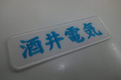 白のアーバンツイル生地に色鮮やかなターコイズの糸で会社名を刺繍した、会社名ワッペンの制作実績。