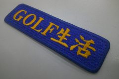 花紺のエンブクロス生地にオレンジ糸でゴルフブランド名をシンプルに刺繍した、文字ワッペンの制作実績。