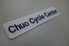 白の生地に黒糸で、自転車屋の屋号を刺繍した、文字ワッペンの加工事例。