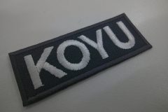 チャコールのツイル生地をベースに白糸で企業名を刺繍した、ミニサイズの文字ワッペンの制作実績。