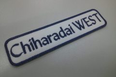 白のツイル生地に濃紺で学校名を刺繍した文字ワッペン。上品な英字書体を使用した事例。