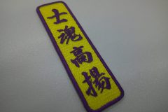 黄色のエンブクロス生地に紫で四文字熟語を刺繍した、縦書きの文字ワッペンの作品事例。
