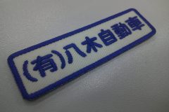 白のツイル生地に自動車販売会社の社名を刺繍した、小さめの文字ワッペンの加工事例。