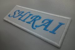 上品な足つきの書体で地域名を水色の糸で刺繍した、上品な印象の文字ワッペンの完成事例。