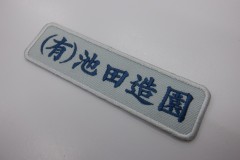 ライトグレーの生地にネイビーの糸で造園名を刺繍した、文字ワッペンの制作事例。