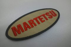 ベージュ色のツイル生地に赤糸でチーム名を刺繍。外周フチには濃紺カラーを使用した文字ワッペン。