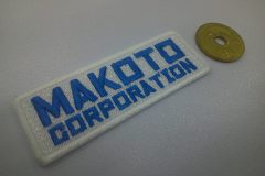 太めのブロック体で、サックブルーの糸で会社名を二段で刺繍した、文字ワッペンの制作実績。