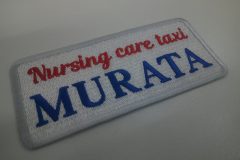 白のエンブクロスに赤糸と青糸で会社名を英字で刺繍した、文字ワッペンの制作事例。