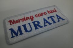 白のエンブクロスに赤糸と青糸で会社名を英字で刺繍した、文字ワッペンの制作事例。