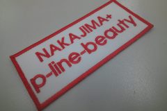 白のツイル生地にサーモンピンクの糸でレーサー名とスポンサー名を刺繍した、文字ワッペンの制作事例。