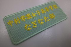 淡い緑のツイル生地に山吹色で学校名と部活動名を刺繍した、二段構成の文字ワッペン。