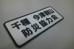 白の生地に黒糸で防災協力会の文字を刺繍。上段には地域名を加工した作品。