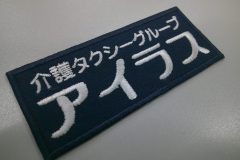 濃紺のツイル生地に白糸で介護タクシーグループ名を文字刺繍した作品。