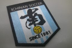 水色と白の縦ストライプを背景に、クラブ名・中央の黒い文字・黄ボール・『SINCE 1981』が配置された盾形のサッカーチームのオリジナルプリントワッペンの制作事例。