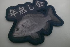 濃紺の背景に精密に描かれた魚と上に『年無し会』の文字が入ったオリジナルプリントワッペンの制作見本。