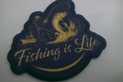 釣り人が魚を釣り上げるモチーフと船のシルエットが描かれ、『Fishing is Life』の文字が入ったオリジナルプリントワッペンの制作事例。