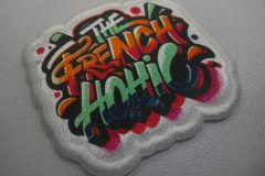 白縁のワッペンに多色のグラフィティ風文字『THE FRENCH HOHIC』が加工されたオリジナルプリントワッペンの制作事例。