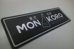 黒地に『MON KORO』の文字とヘラのモチーフが描かれた飲食店のオリジナルプリントワッペンの制作事例。