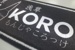 黒地に『MON KORO』の文字とヘラのモチーフが描かれた飲食店のオリジナルプリントワッペンの制作事例のあっぷ。