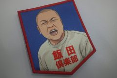 赤い縁に、強い表情の人物と『飯田倶楽部』の文字が描かれたオリジナルプリントワッペンの制作見本。