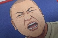 赤い縁に、強い表情の人物と『飯田倶楽部』の文字が描かれたオリジナルプリントワッペンの制作見本のアップ。