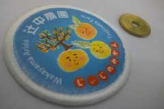 青地にみかんの木と3つの笑顔のみかんキャラクターが描かれた円形のオリジナルプリントワッペンの制作見本。