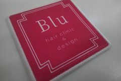 赤地に白い二重枠と『Blu hair clinic & design』の文字が配置されたシンプルな四角形のオリジナルプリントワッペンの制作事例。